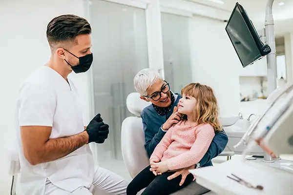 A cute little girl sitting in dentist chair before a routine dental procedure, accompanied by her grandmother.