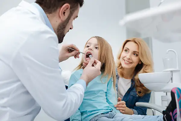 An attentive mom sitting with her young daughter while a dentist inspects the girl's teeth.