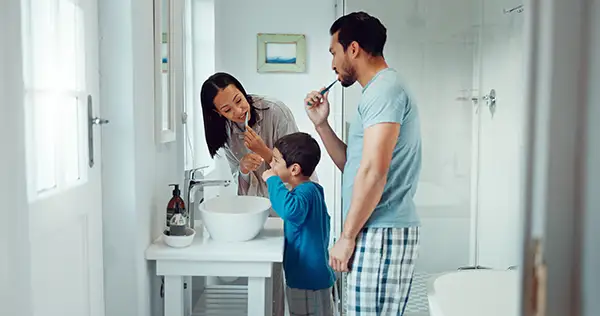 A family of three brushing their teeth together in the bathroom mirror, practicing good dental care.